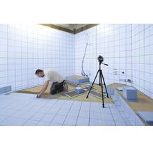 Een man legt tegels in een badkamer, waarbij een laserwaterpas wordt gebruikt om de uitlijning te garanderen.