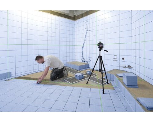 Een man legt tegels in een badkamer, waarbij een laserwaterpas wordt gebruikt om de uitlijning te garanderen.