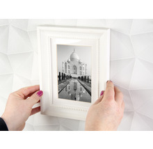 Handen houden een witte fotolijst vast met een zwart-witfoto van de Taj Mahal voor een muur