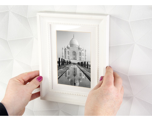 Handen houden een witte fotolijst vast met een zwart-witfoto van de Taj Mahal voor een muur