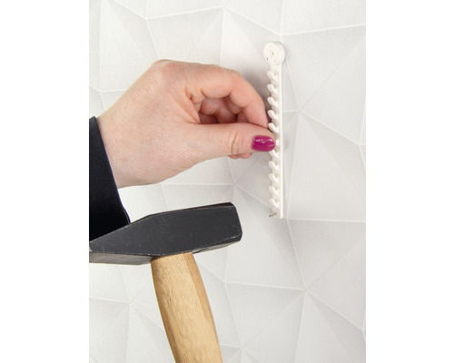 Iemand bevestigt een fotolijsthaak met een hamer aan een muur