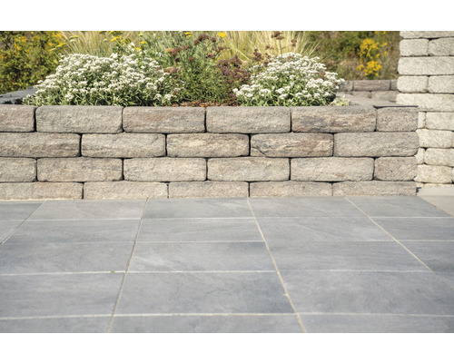 Tuinmuur van stenen blokken met bloemen en bestrating