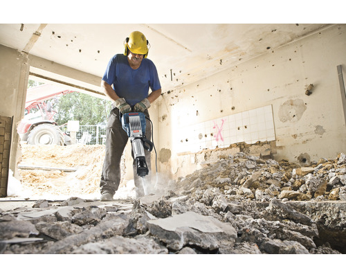 Een bouwvakker gebruikt een breekhamer om metselwerk in een ruimte af te breken.