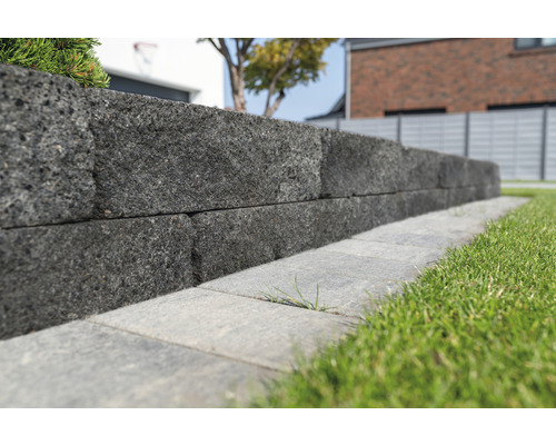 Een muur van grijze stenen in een tuin.