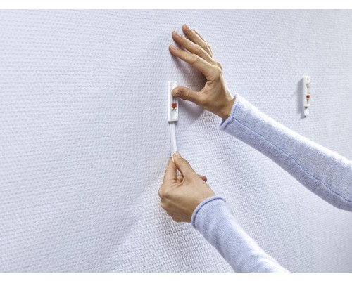 Persoon bevestigt een plakhaak aan een muur.