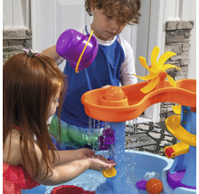 Kinderen spelen met een waterspeeltafel buiten met glijbanen, trechters en een waterrad.