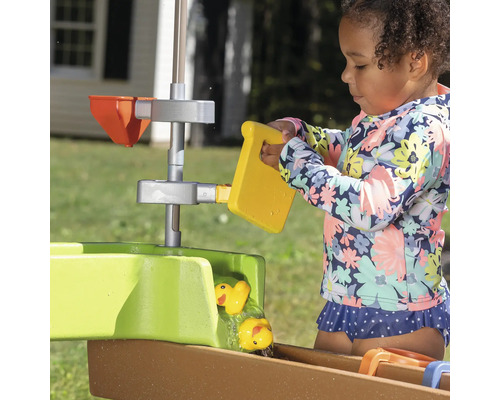Meisje speelt met een waterspeeltafel met gele eenden en emmer in de tuin