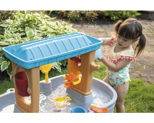 Klein meisje speelt met een water- en zandtafel in de tuin