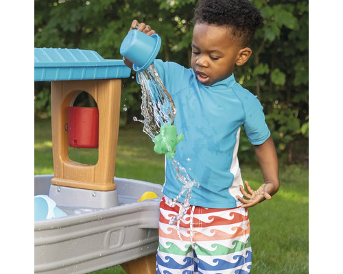 Jongen speelt met een waterspeeltafel buiten door water uit een beker te gieten
