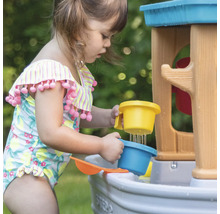 Een kind speelt met een Step2 waterspeeltafel buiten en giet water met een beker.