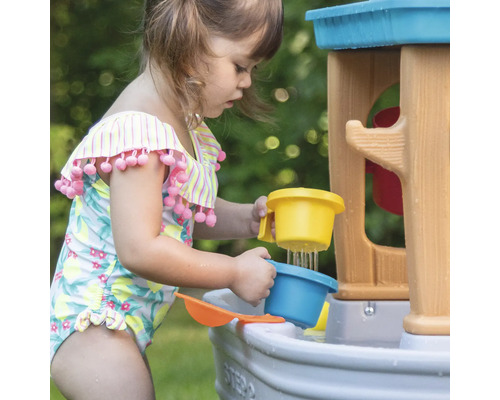 Een kind speelt met een Step2 waterspeeltafel buiten en giet water met een beker.