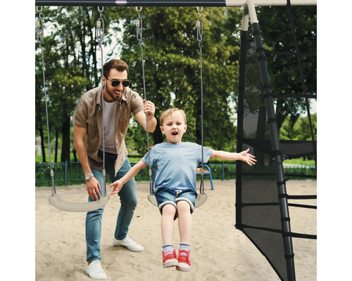 Vader duwt kind op een schommel aan een speeltoren.