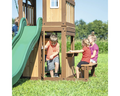 Houten speelhuis met glijbaan en tafel met bank in de tuin
