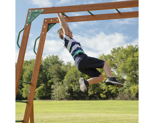 Jonge hangt aan een kinderschommel in de tuin.