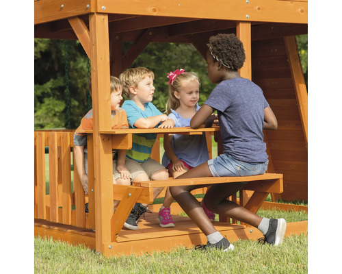 Kinderen spelen op een houten speelplaats met picknicktafel.