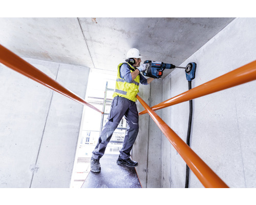 Een bouwvakker boort met een boorhamer een gat in een betonnen muur.