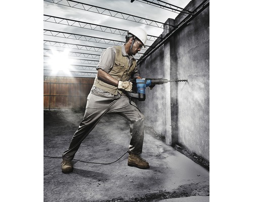 Een bouwvakker boort met een boorhamer een gat in een betonnen muur.