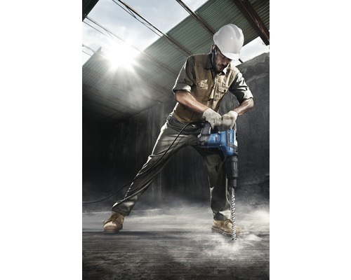 Een bouwvakker met veiligheidshelm boort met een breekhamer in de grond.