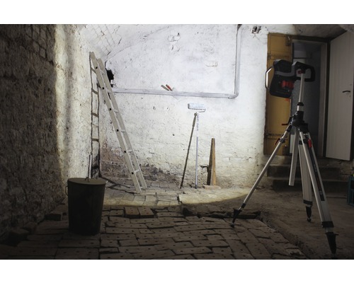 Kelderruimte met ladder, emmer, verfroller en bouwlamp op statief