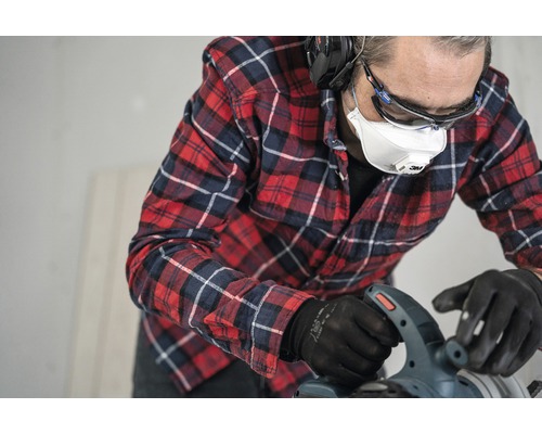 Ambachtsman met veiligheidsmasker, veiligheidsbril, gehoorbescherming en handschoenen aan het werk met een zaag