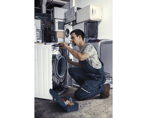 Een man repareert een wasmachine met gereedschapskist