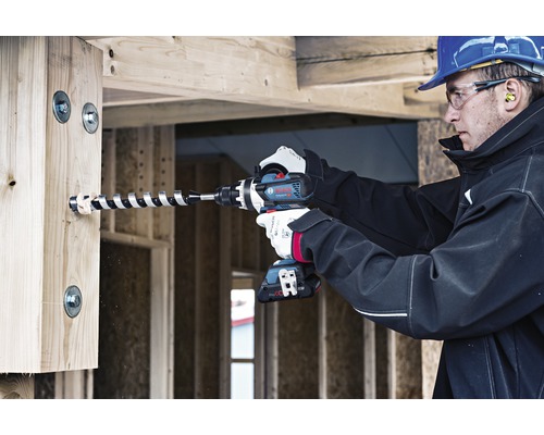 Een man boort met een accuboormachine een gat in een houten balk.