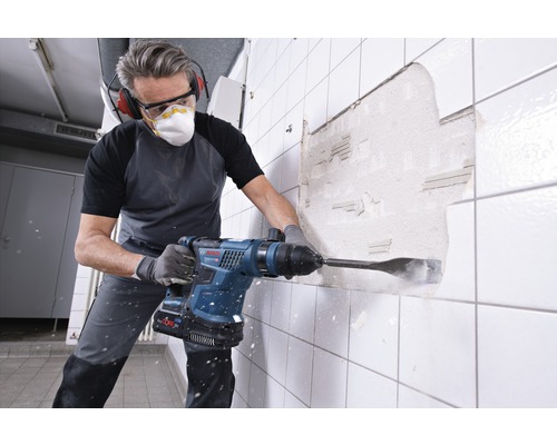 Man werkt met een drilhamer aan een muur met tegels.