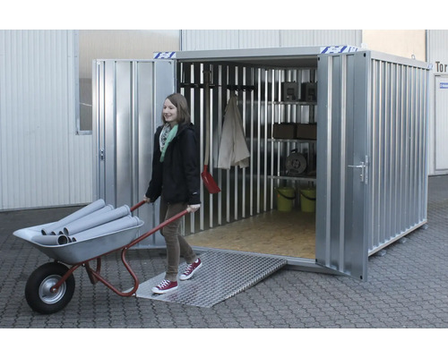 Stalen container met helling en rekken. Een vrouw duwt een kruiwagen met buizen in de container.
