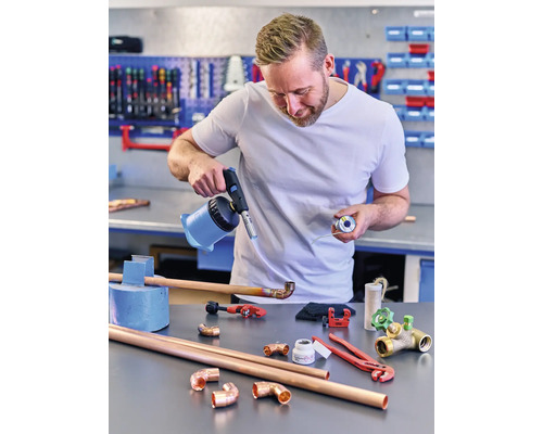 Man soldeert koperen buizen met een gasbrander en soldeertin op een werkbank.