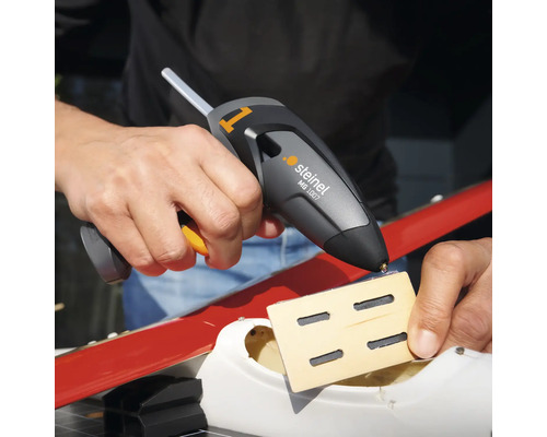 Een persoon gebruikt een Steinel MG 1007 lijmpistool om een stuk hout vast te lijmen.