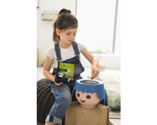 Meisje vult plantenbak in de vorm van een gezicht met gazonzaden, houdt zaadomslag vast, bio keurmerk