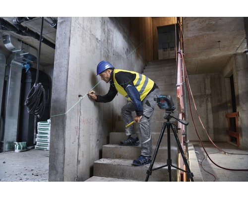 Een bouwvakker gebruikt een lijnlaser op een bouwplaats om een rechte lijn op een betonnen muur te markeren.