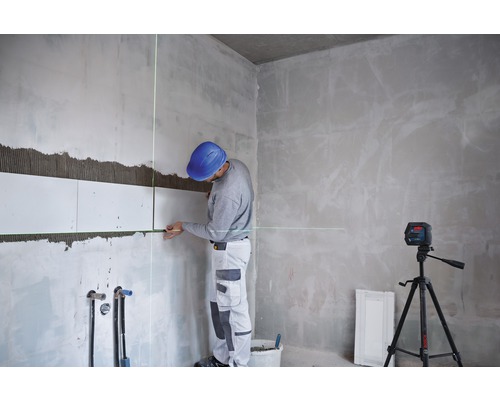 Een man legt tegels met een lijnlaser in een kamer.