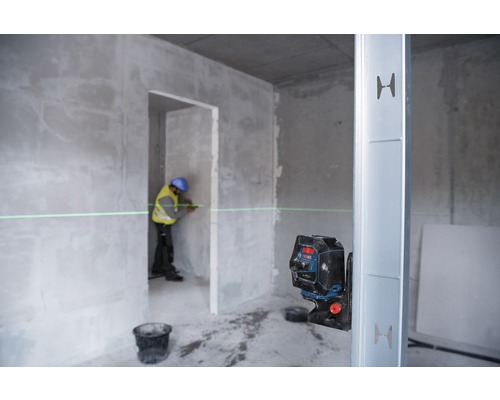 Een arbeider gebruikt een lijnlaser in een casco om een rechte lijn op een muur te markeren.