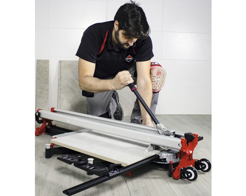 Een vakman knielt en snijdt een tegel met een tegelsnijder.