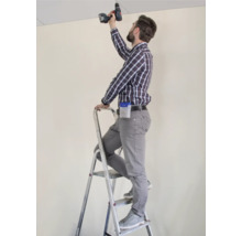 Ambachtsman op een ladder die met een accuschroevendraaier aan een plafond werkt