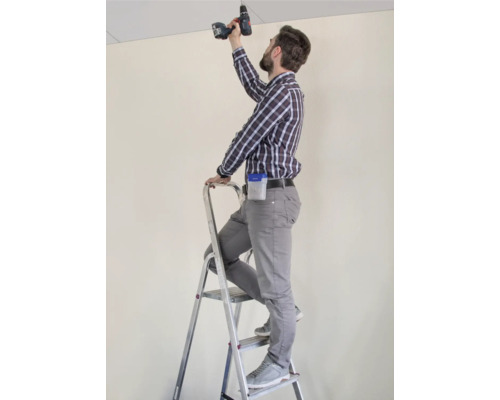 Ambachtsman op een ladder die met een accuschroevendraaier aan een plafond werkt