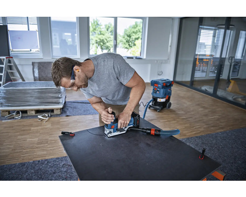 Een vakman werkt met een groeffrees aan een plaat, een stofzuiger staat klaar.