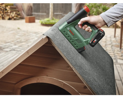 Een persoon bevestigt dakleer met een accutacker op een houten huis.