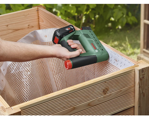 Een persoon bevestigt met een accus tacker vlies in een verhoogde tuinbak.