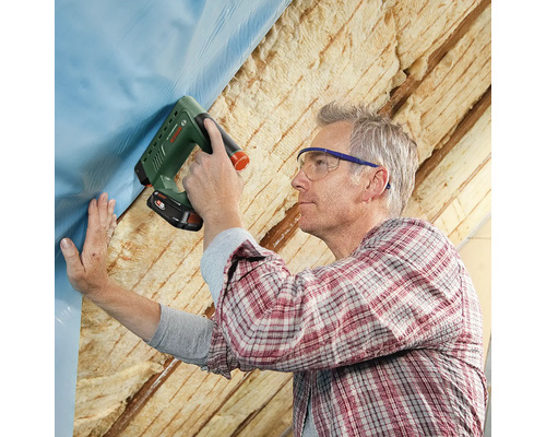 Een man bevestigt folie met een tacker aan een dakconstructie.