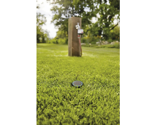 Scene met een irrigatiesensor in het gras en een waterkraan op de achtergrond.