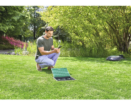 Man bedient tuinbewateringssysteem met smartphone in de tuin.