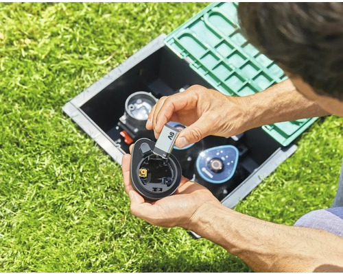 Persoon plaatst een batterij in een bewateringscomputer in de tuin