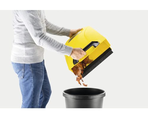 Een persoon leegt een gele bladverzamelaar in een zwarte afvalemmer.