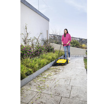 Vrouw veegt met een veegmachine een voetpad schoon van bladeren en bloemen