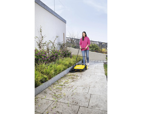 Vrouw veegt met een veegmachine een voetpad schoon van bladeren en bloemen