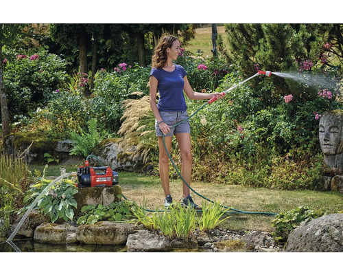 Vrouw besproeit tuin met tuinpomp en tuinslang