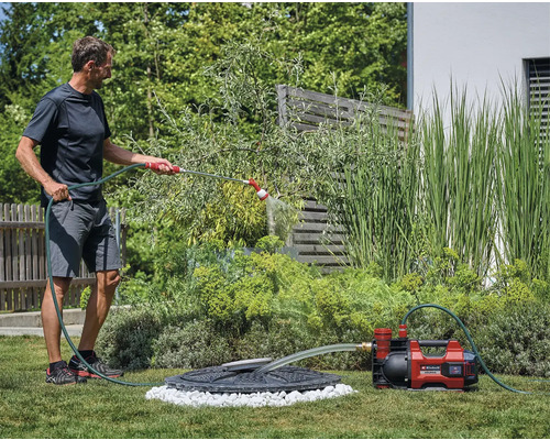 Man besproeit tuin met tuinpomp en slang