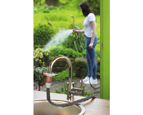 Tuinscène met kraan en aangesloten tuinslang, op de achtergrond een vrouw die planten water geeft